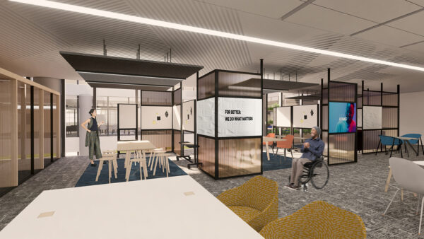 Wheelchair user in the foreground in office with table at the front and room dividers behind. High table and stools to the left.