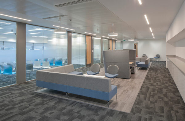 Communal seating area in the centre of the room with separating wooden flooring, carpeting and selection of seat options either chairs or sofas.