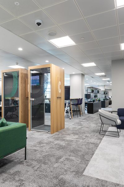 Office call pod on grey carpet with green sofa in the foreground