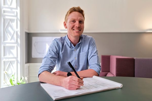 Man in blue shirt with pen in hand writing on notebook