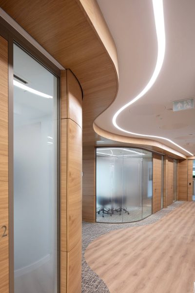 A corridor with curved wooden walls and meeting rooms with frosted glass