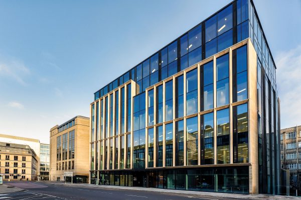 A view from the corner of building with dark glass panels and light metal partitions in between panels.