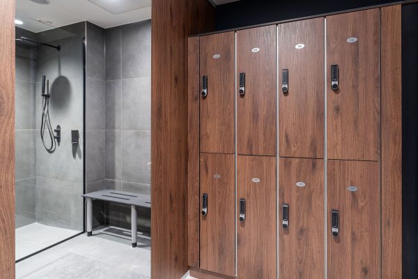 A changing room with dark oak lockers and grey tiles in the shower area.