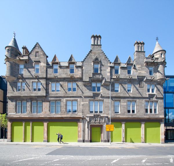 An traditional Scottish buildings with towers, with the bottom floor windows being boarded up.